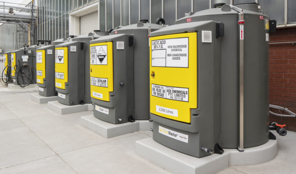 A row of grey and yellow tanks in front of a building.