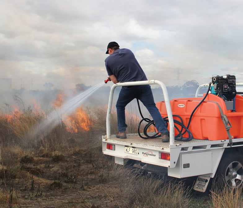 A man spraying a fire from the back of a truck.