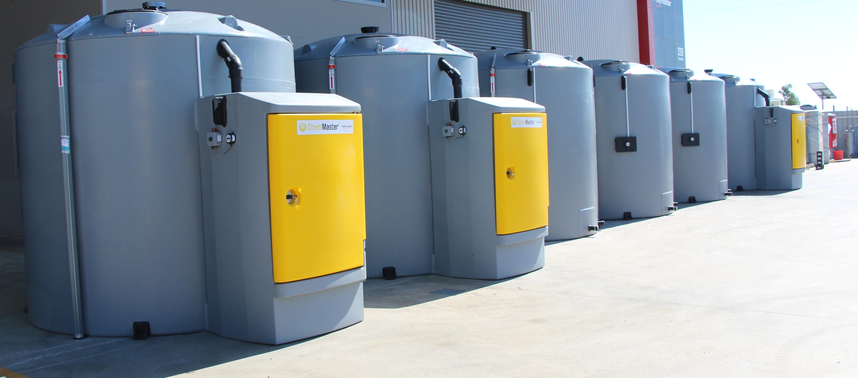 A row of grey and yellow tanks in front of a building.