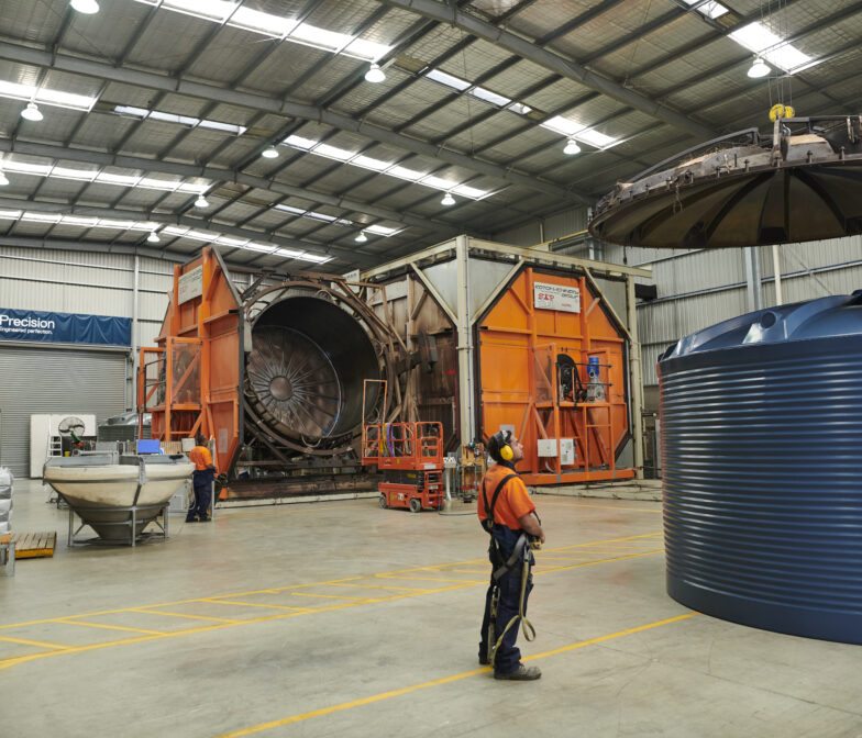 Polymaster worker inspecting a large blue poly water tank inside the manufacturing facility