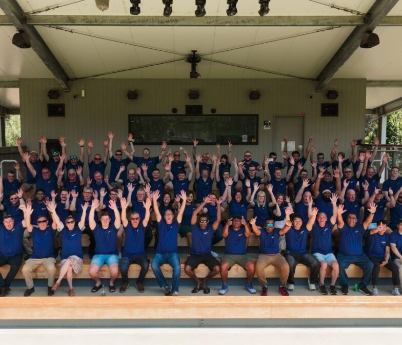 The full Polymaster team in matching blue company shirts raising their hands and smiling for a group photo at an outdoor staff event in Australia