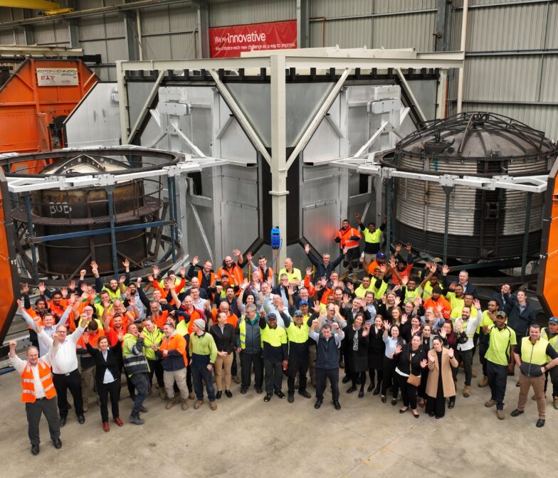Polymaster manufacturing and office staff waving together on the factory floor surrounded by large industrial tank moulding equipment at their Australian production facility