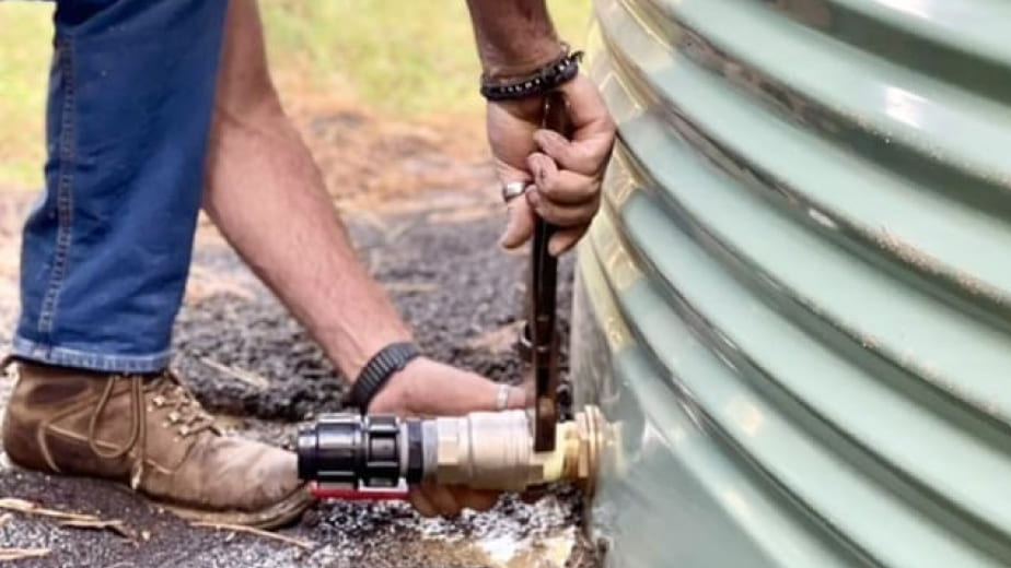 A farmer tightening the brass outlet of a water tank